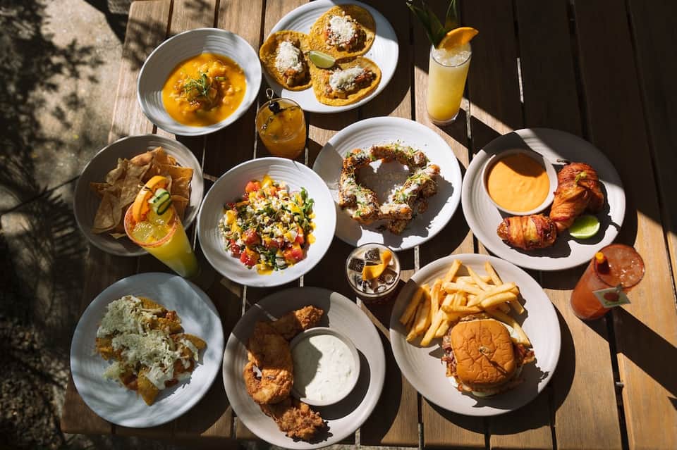 Overhead view of gourmet dishes including soup, pastries, salads, seafood, and beverages on wooden deck