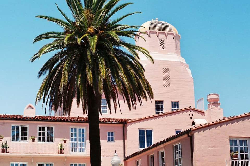 Pink Mediterranean-style building with palm tree and distinctive tower under blue sky