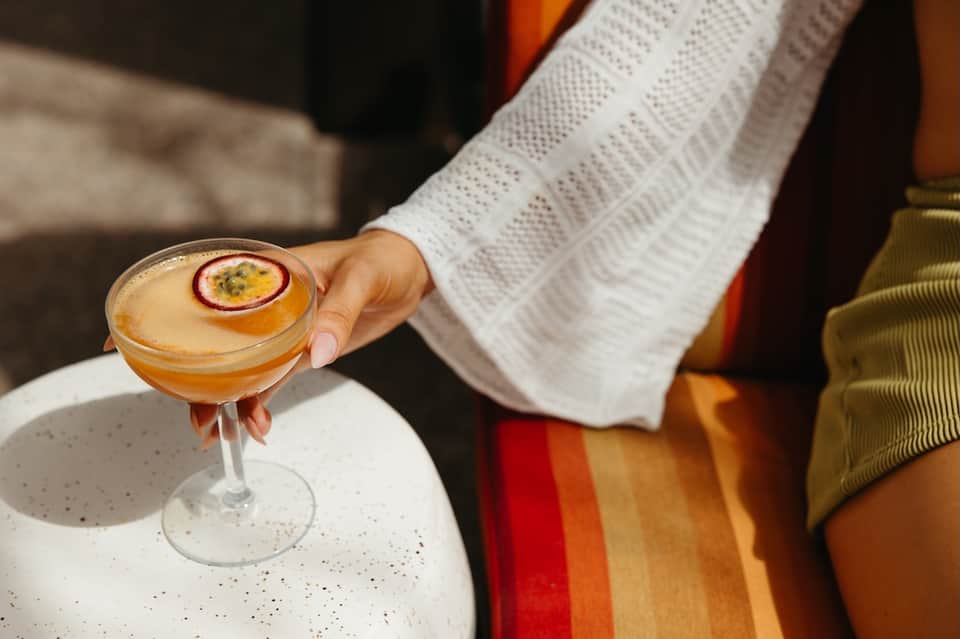 Elegant cocktail with passion fruit garnish held by person in white sweater at outdoor venue