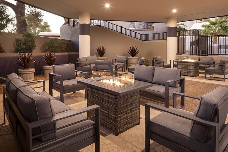 Covered outdoor patio with fireplace, gray seating, potted plants, and metal railings