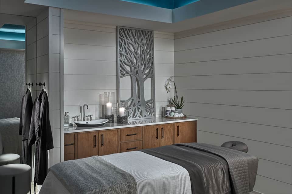 Spa treatment room with massage table, wooden vanity, mirror, and blue ceiling accent