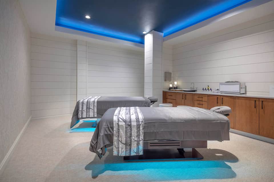 Spa treatment room with two massage beds, blue accent lighting, and wooden cabinetry