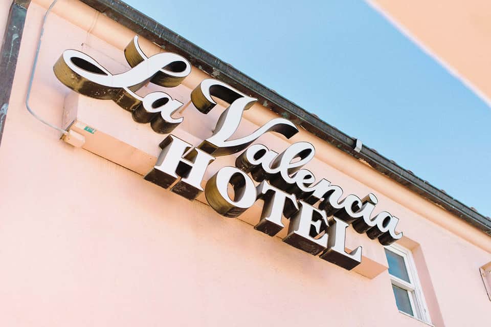 Upscale hotel sign with white cursive lettering and brass accents on pink building facade