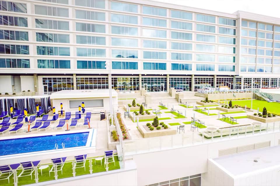 Modern hotel rooftop with outdoor pool, lounge areas, green spaces, and waterfront city views