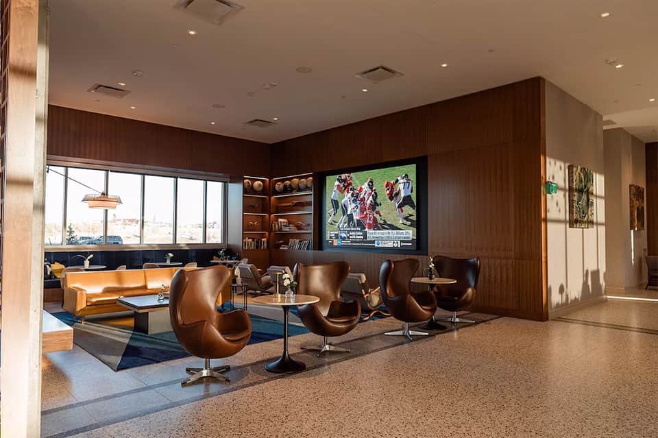 Modern lounge area with brown leather furniture, dark wood paneling, and TV on wall