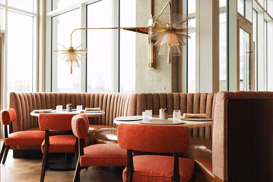 Fine dining room with taupe booths, gold pendant lights, and floor-to-ceiling windows