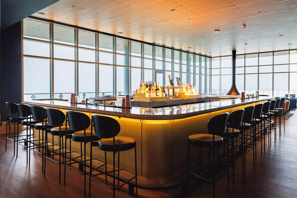 Modern bar with curved counter, black and yellow stools, and floor-to-ceiling windows