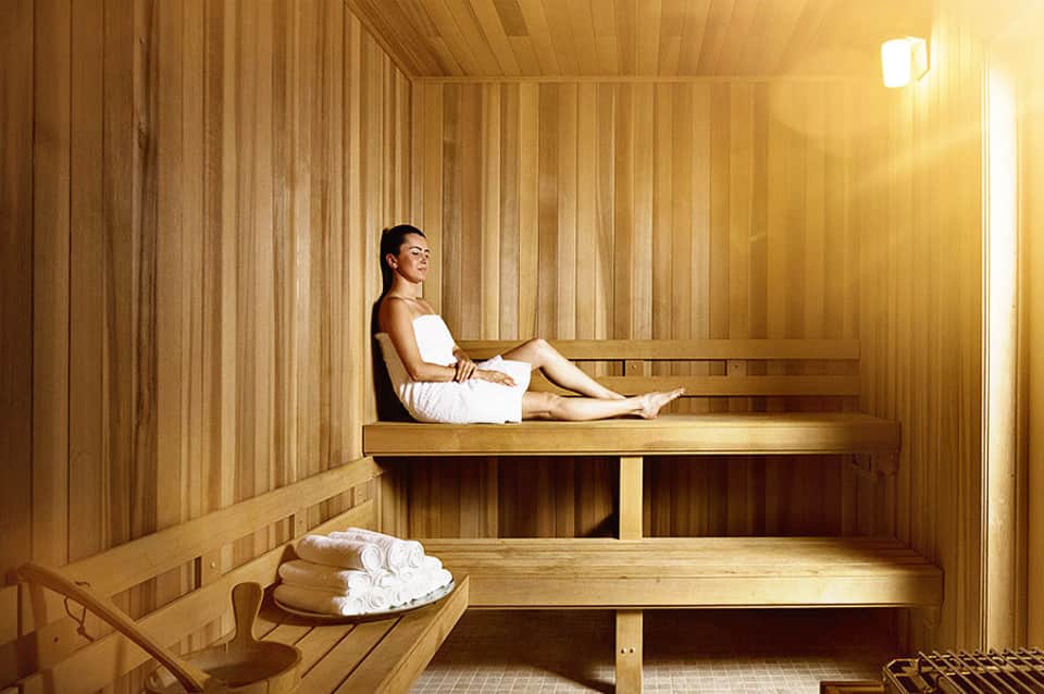 Woman relaxing on wooden bench inside a traditional sauna with warm cedar wood paneling
