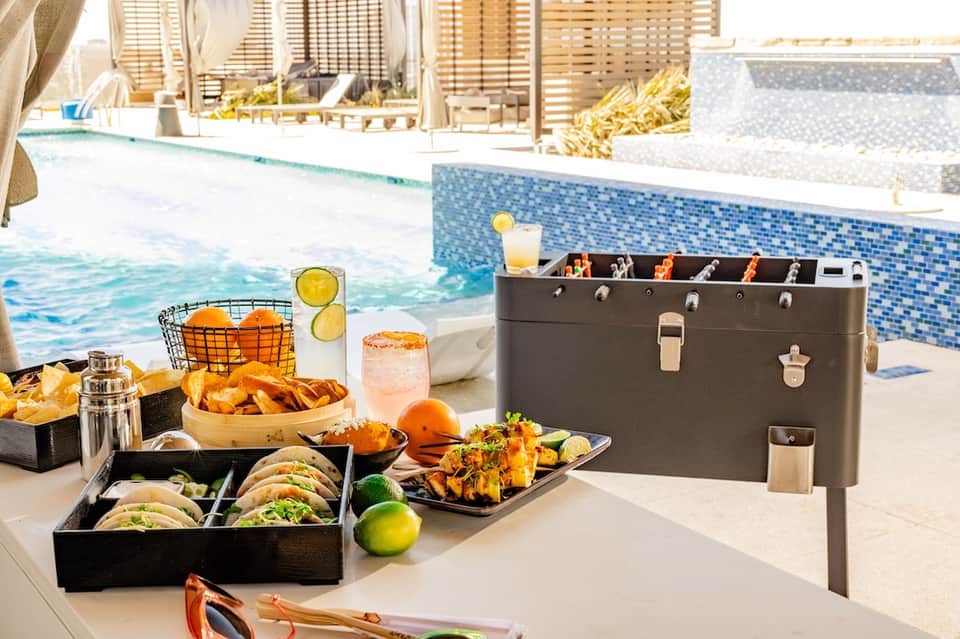 Poolside barbecue setup with tacos, grilled food, drinks, and lounge area