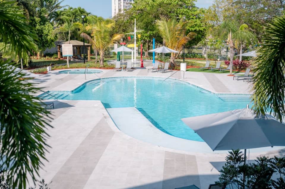 Large outdoor pool surrounded by lush tropical vegetation and white umbrellas at resort