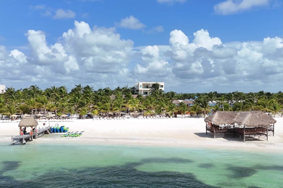 Aerial view of pristine white sand beach with palm trees, thatched structures, and clear turquoise water
