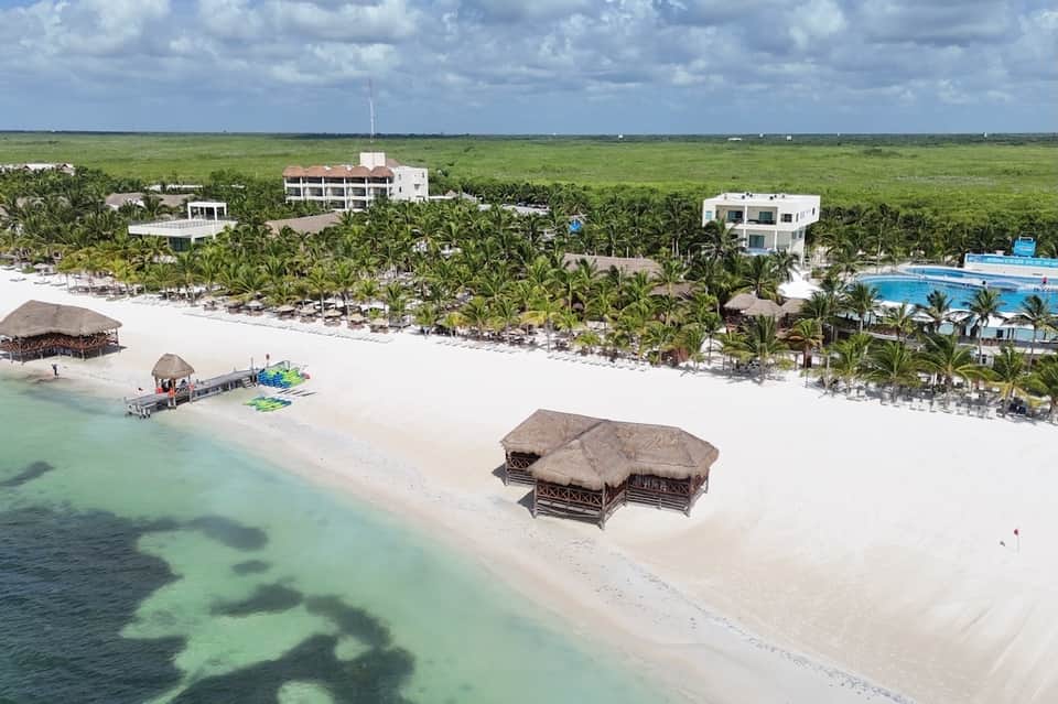 Beachfront resort aerial view with white sand, thatched structures, pools, and tropical landscaping