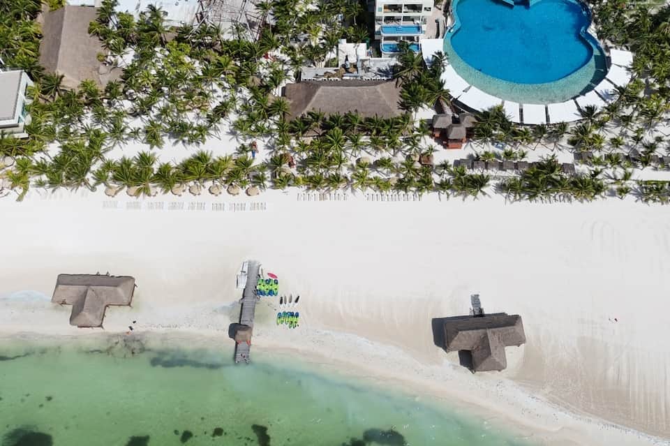 Aerial view of beachfront resort with palm trees, pool, and white sand beach