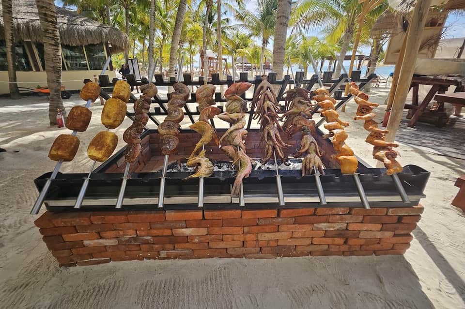 Beach barbecue display with grilled meats and seafood on skewers over open flames