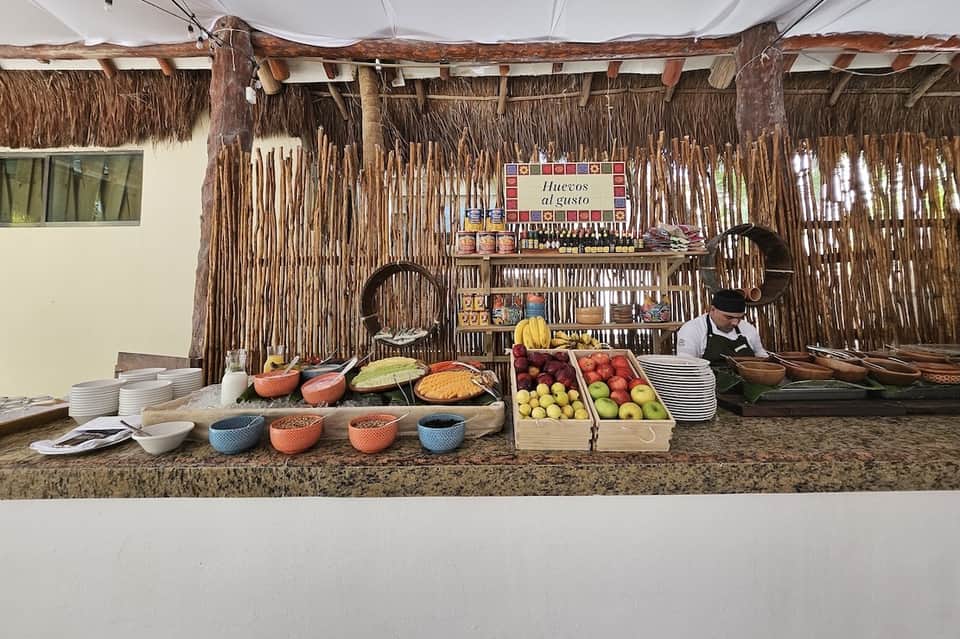 Beach bar with thatched roof, fresh fruits and foods displayed, staff preparing meals, rustic tropical setting