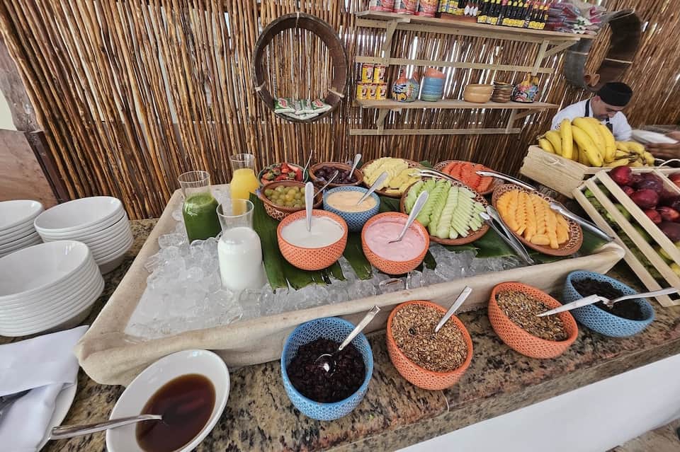 Tropical breakfast buffet spread with fresh fruits, juices, cereals, and breads on rustic wooden table