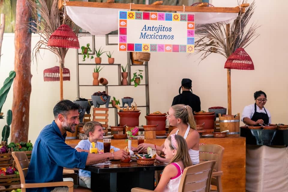 Mexican restaurant interior with colorful decor, hanging lamps, potted plants, and family dining