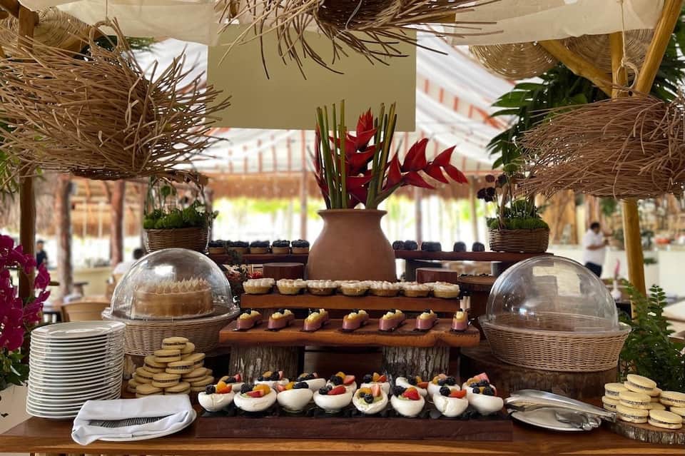 Elegant outdoor buffet display with covered food domes, decorative potted flowers, tropical arrangements, and plated appetizers