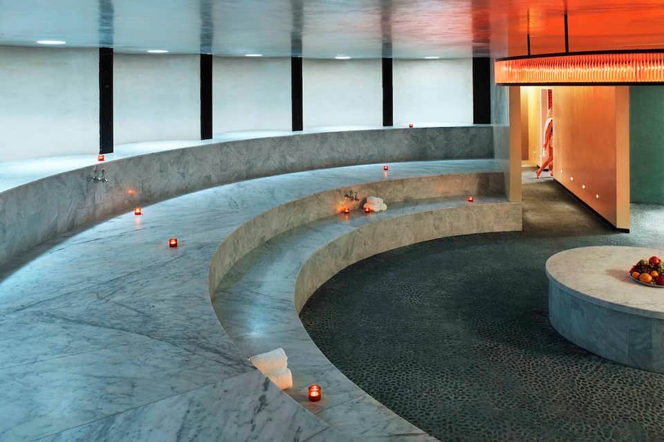 Modern spa relaxation area with curved marble benches, ambient lighting, and candlelight