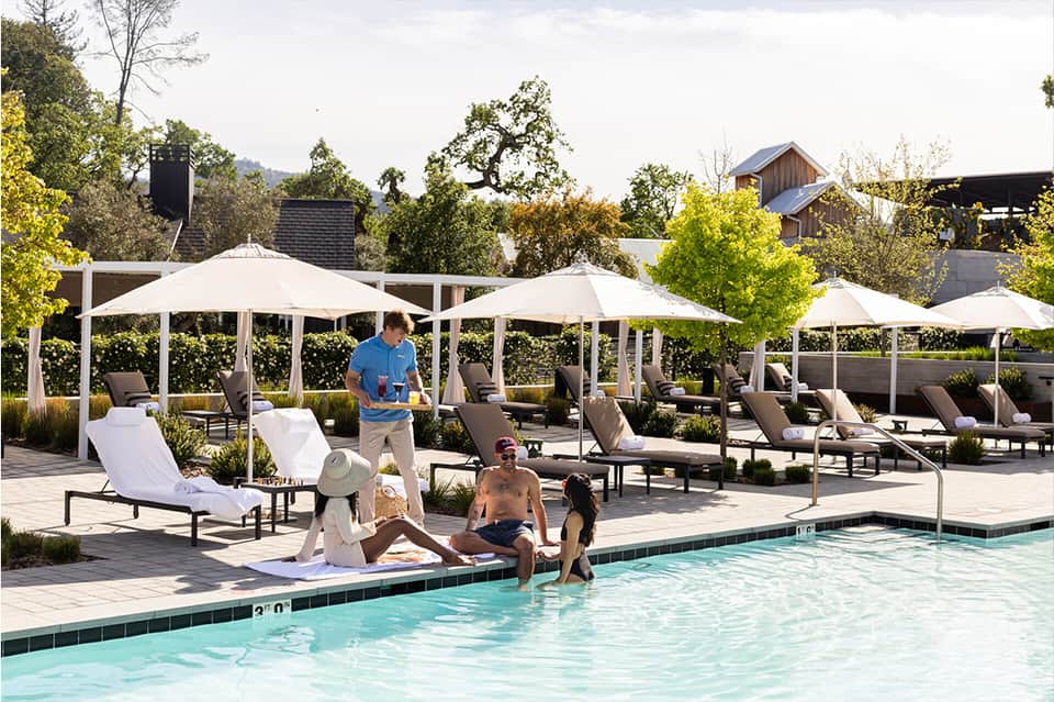 Resort pool area with white umbrellas, lounge chairs, and mountain views