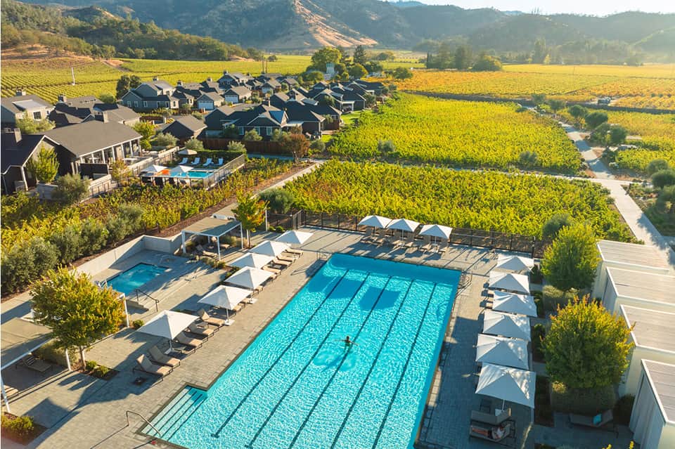 Aerial view of resort with swimming pool, vineyard landscape, mountains, and residential buildings