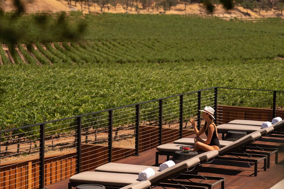 Woman relaxing on vineyard terrace with view of rolling green grapevines below