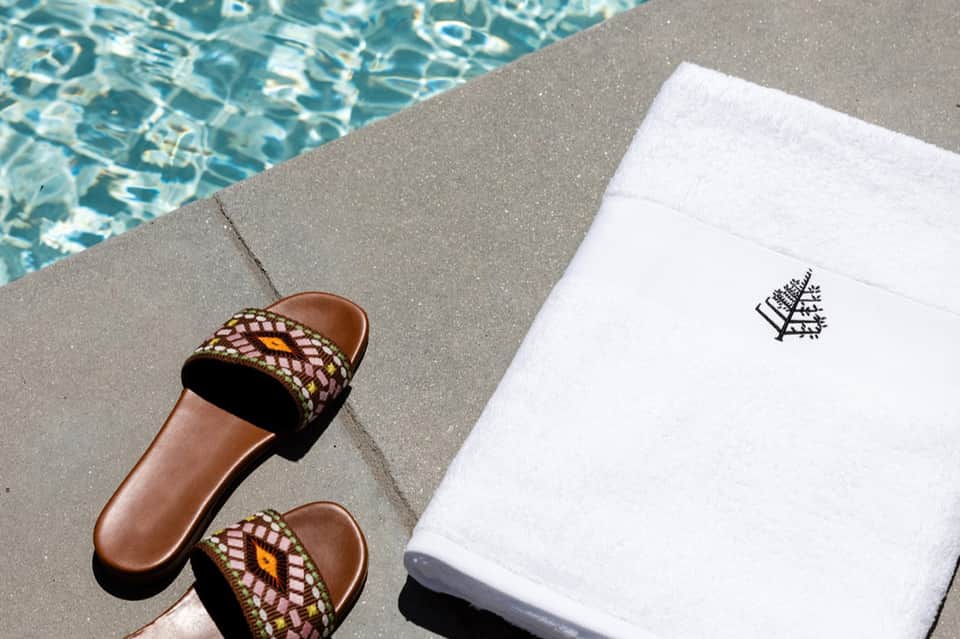 Pool deck detail with decorative sandals and white towel with logo beside turquoise water