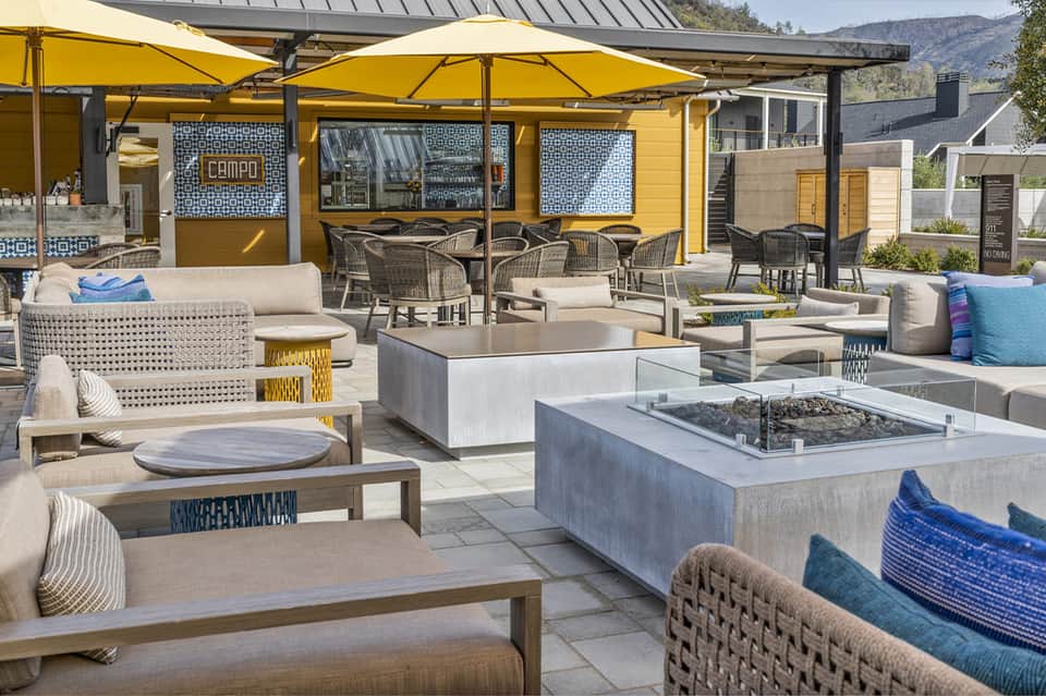 Outdoor resort patio with fire pit, lounge seating, yellow umbrellas, and mountain views