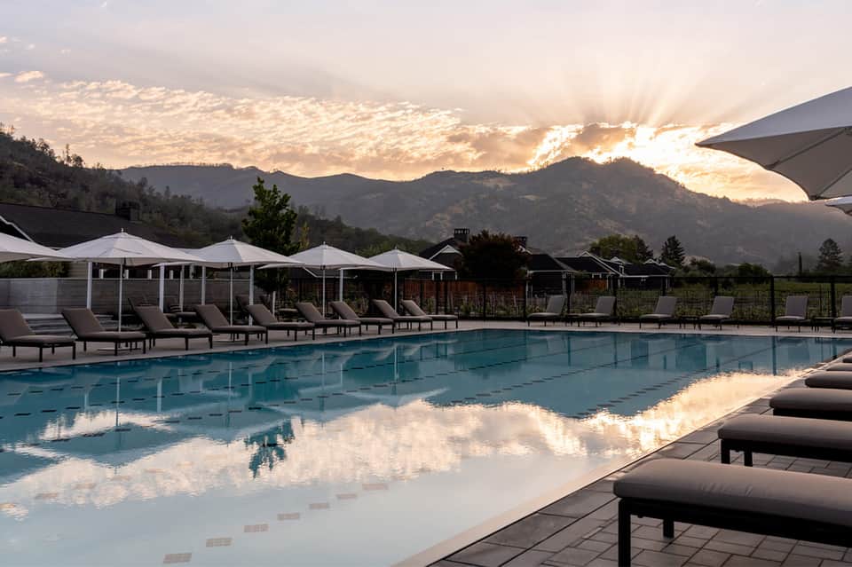 Mountain resort pool at sunset with white cabanas, lounge chairs, and dramatic sky