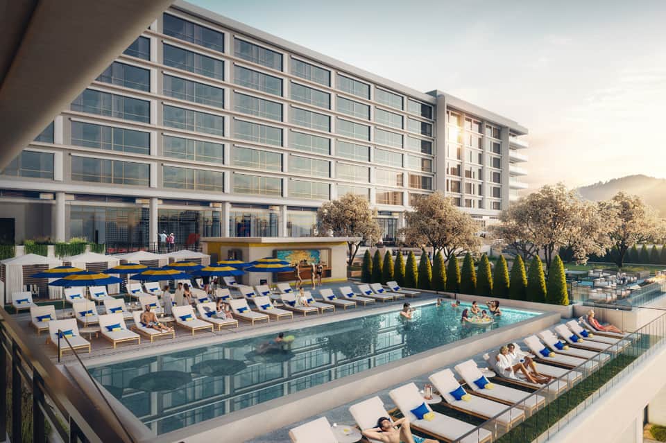 Resort exterior with pool, blue umbrellas, lounge chairs, and modern multi-story building with mountain views