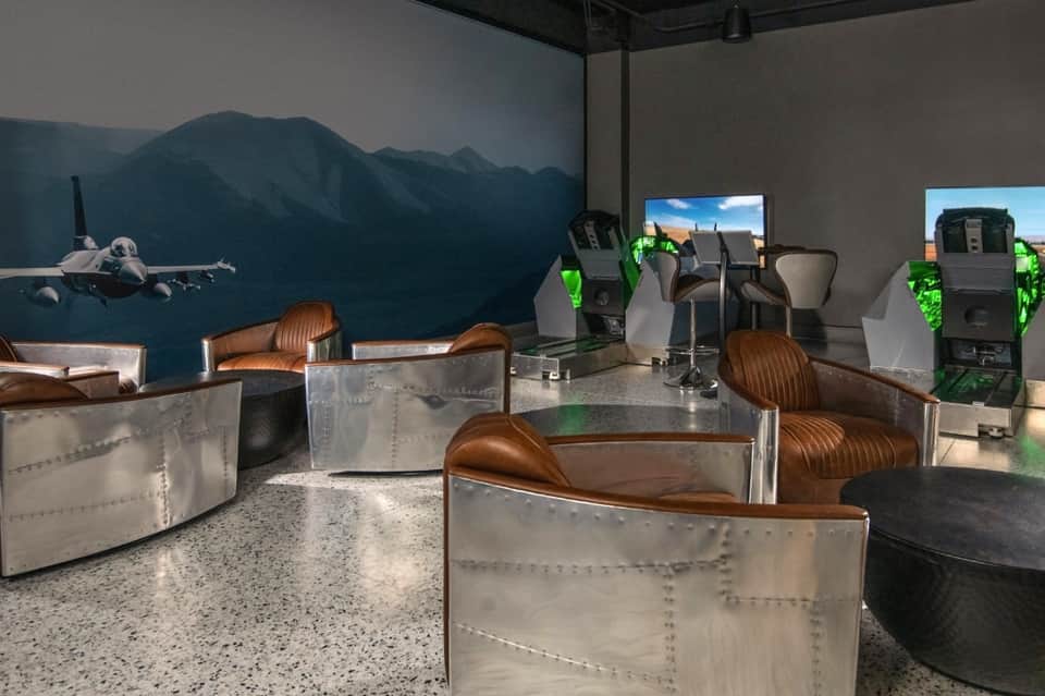 Gaming lounge with airplane-themed seating pods, flight simulator screens, and mountain mural