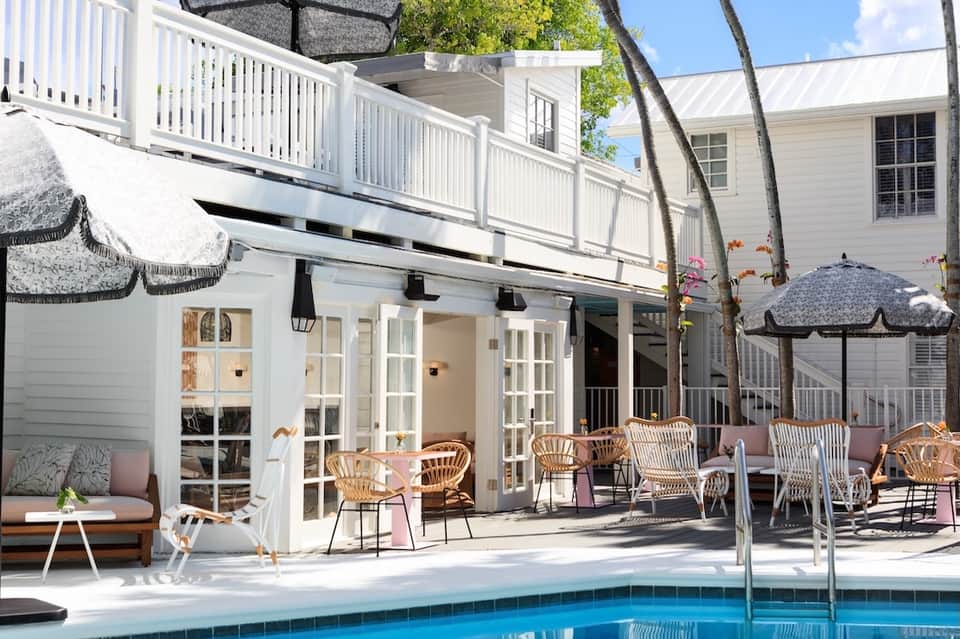 Waterfront resort deck with dining area, wicker chairs, pool, and palm trees