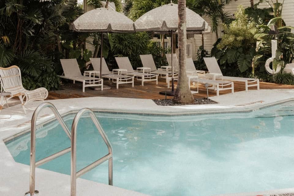 Tropical pool area with white umbrellas, lounge chairs, palm trees, and wooden deck