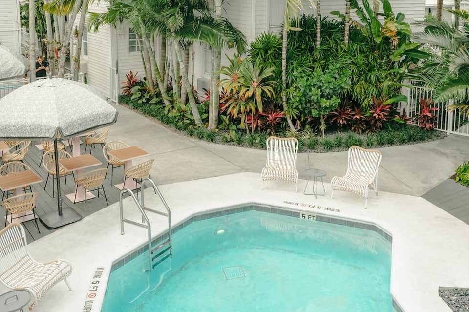 Tropical courtyard pool with white loungers, palm plants and white residential buildings