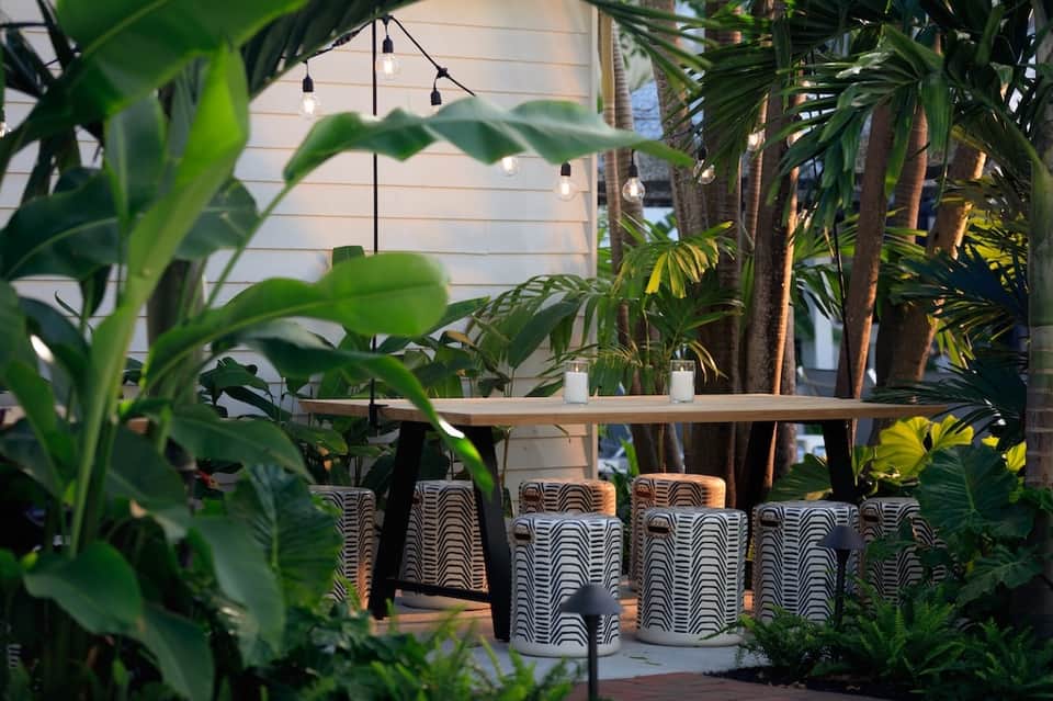 Outdoor dining area surrounded by tropical plants with wooden table and patterned chairs