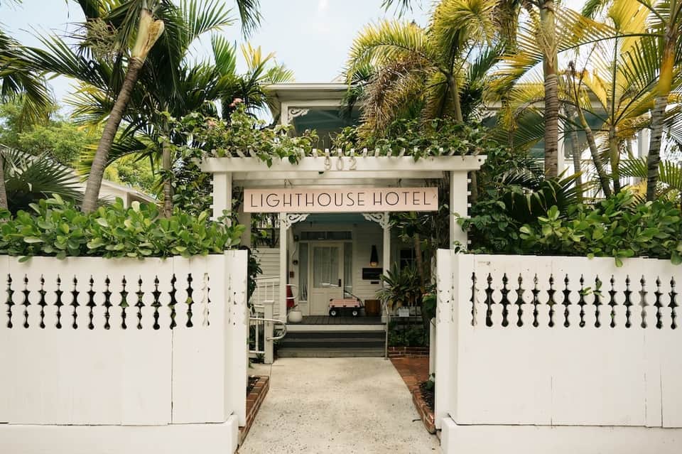 Tropical-themed hotel entrance with white picket fence, palm trees, and covered walkway