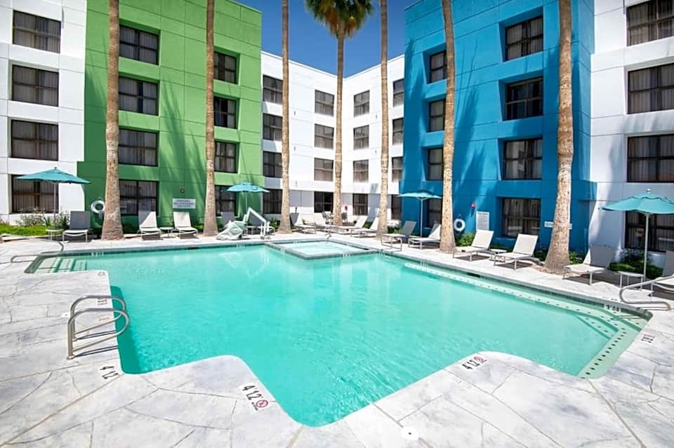 Outdoor pool surrounded by colorful building facades in green, blue, and white with palm trees
