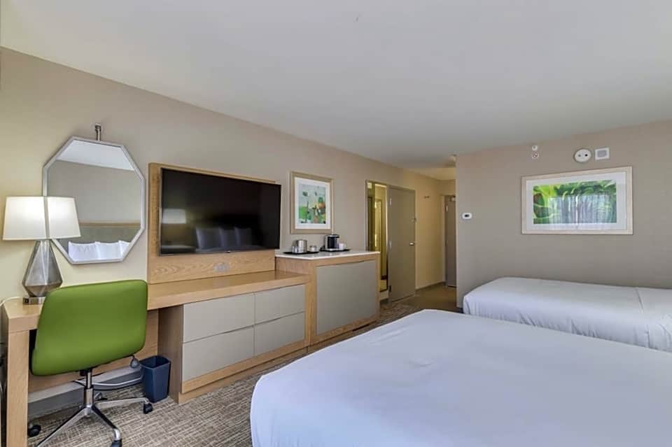 Hotel room with two queen beds, flat-screen TV, desk with green chair, and bathroom