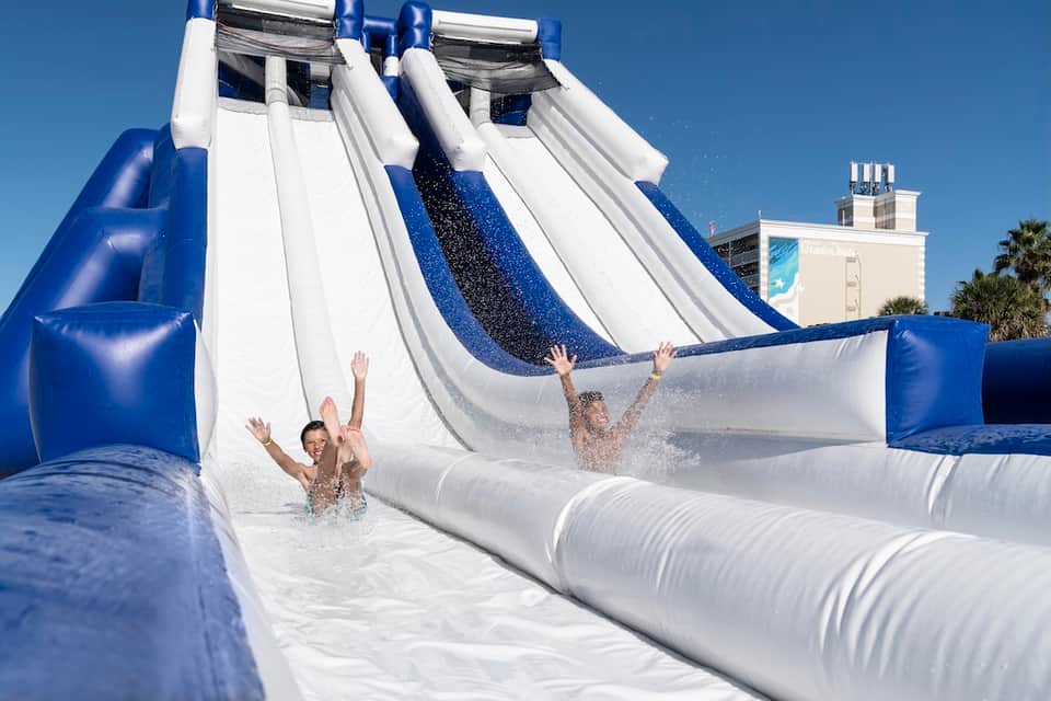 Children sliding down blue and white inflatable water slide into splash pool at resort