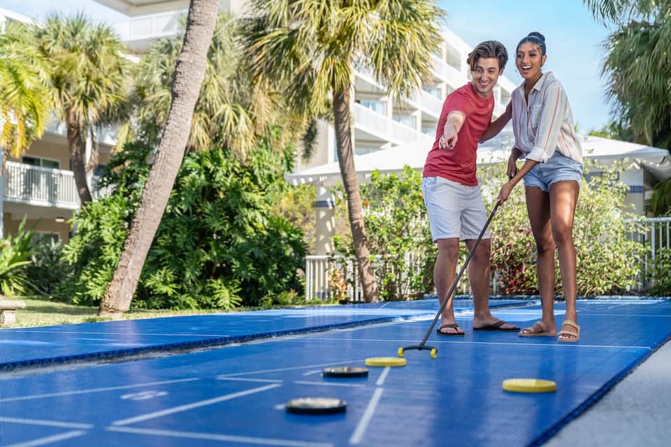 Couple playing mini golf on blue course with palm trees and resort buildings in background