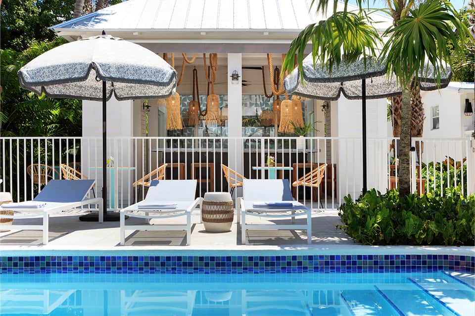 Resort poolside lounge with white umbrellas, loungers, and coastal architectural style building