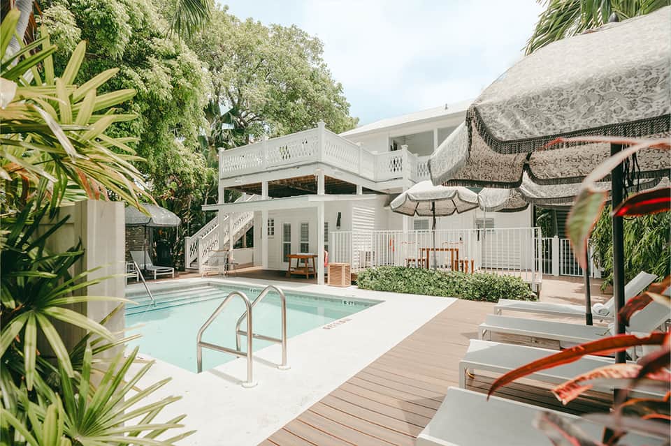 Resort pool area with white cabanas, thatched umbrellas, tropical landscaping and deck seating