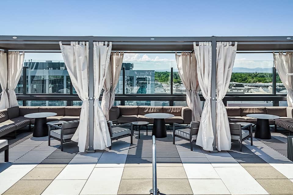 Rooftop lounge with white curtained cabanas, black furniture, and mountain landscape views