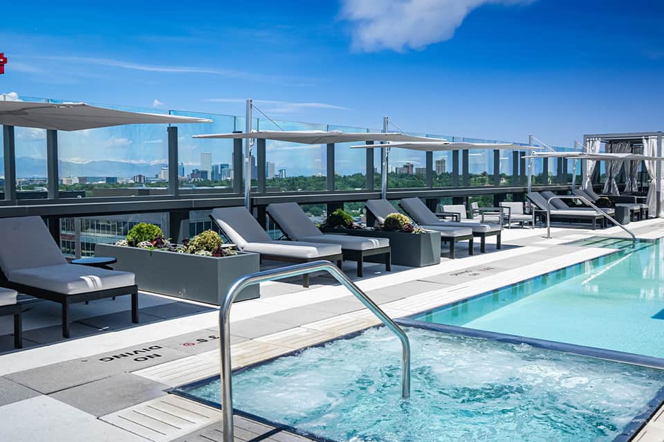 Rooftop pool and spa with lounge chairs, city skyline views, and glass safety barriers
