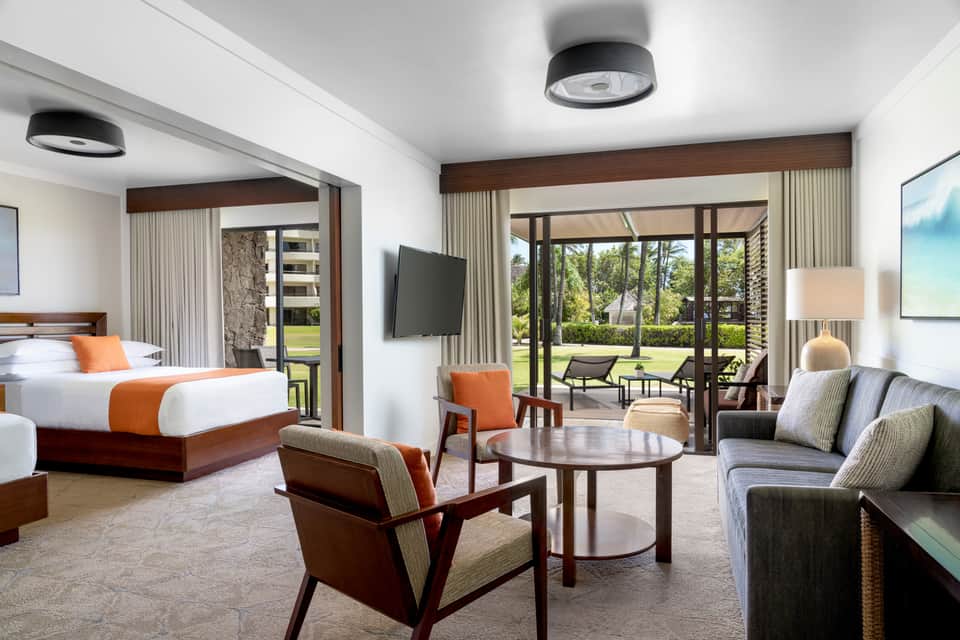 Luxury hotel suite with bed, seating area, wood accents, and sliding doors opening to patio view