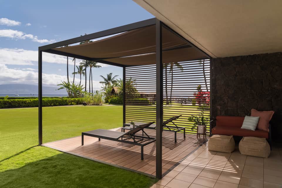 Residential patio with pergola, lounge seating, and manicured lawn overlooking water
