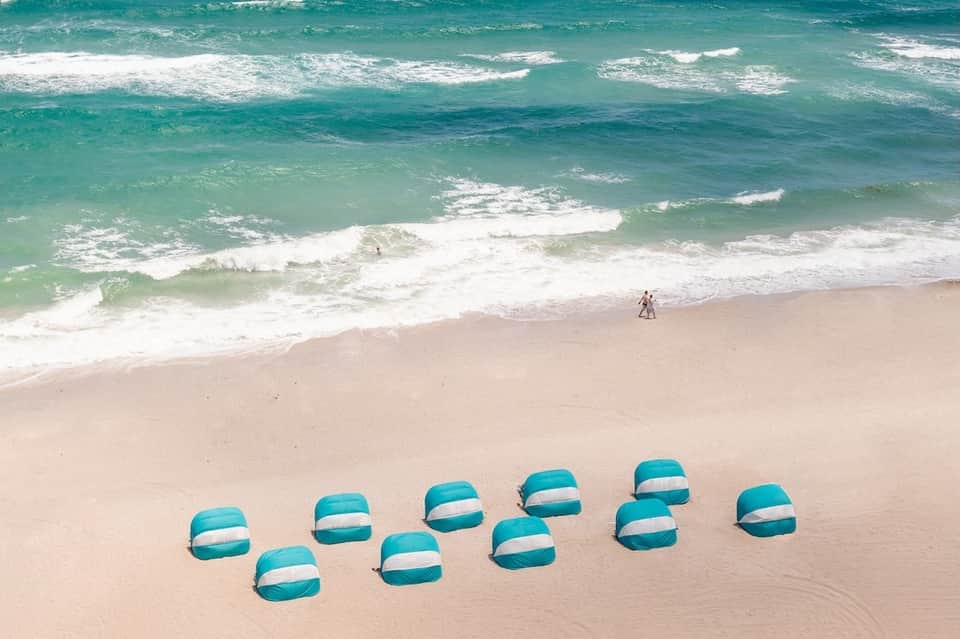 Aerial view of beach umbrellas on sand with turquoise ocean and surfers in the water