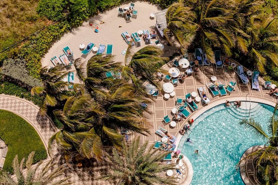 Aerial view of resort pool deck with lounge chairs, umbrellas, and manicured palm trees
