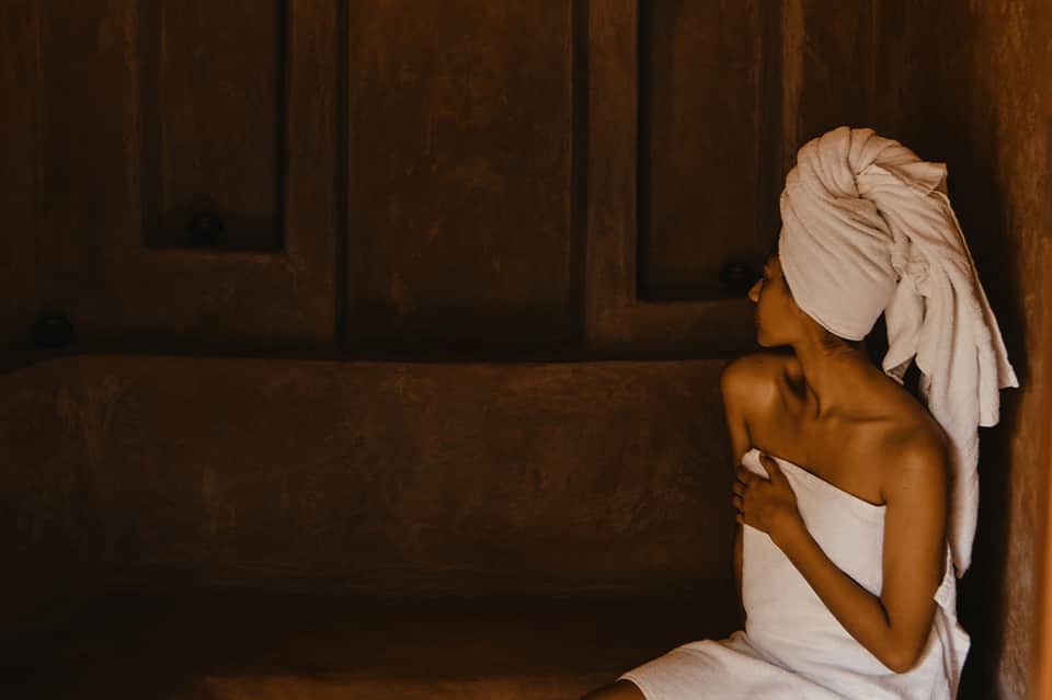Woman in spa with white towel wrap and turban in dark wooden sauna or steam room