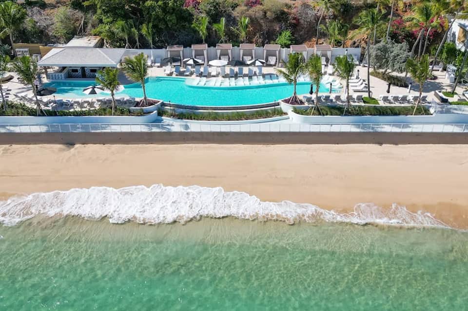 Beachfront resort pool with turquoise water, lounge chairs, and ocean waves in foreground